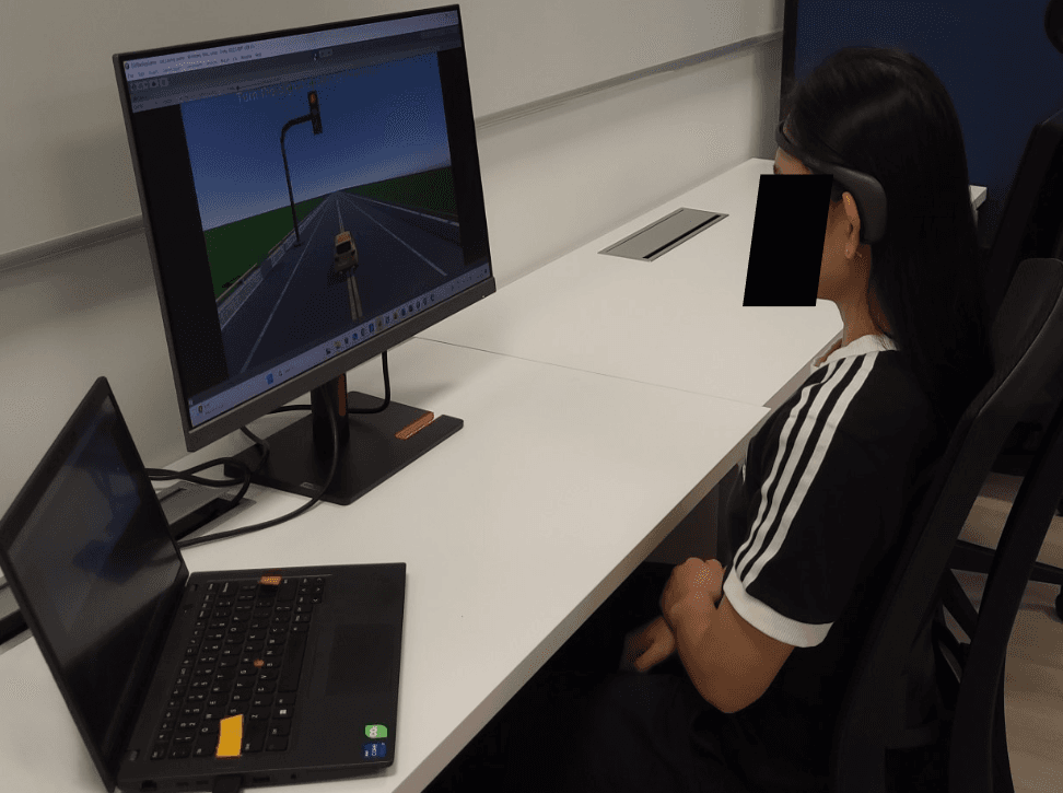 A person wearing a brain-computer interface (BCI) headband while sitting at a desk and interacting with a driving simulation displayed on a computer monitor.