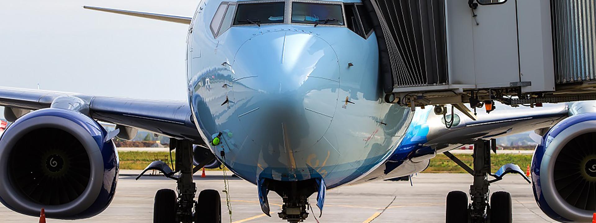 Front view of a commercial jet docked at an airport terminal gate with a connected passenger boarding bridge, representing aircraft ground operations.