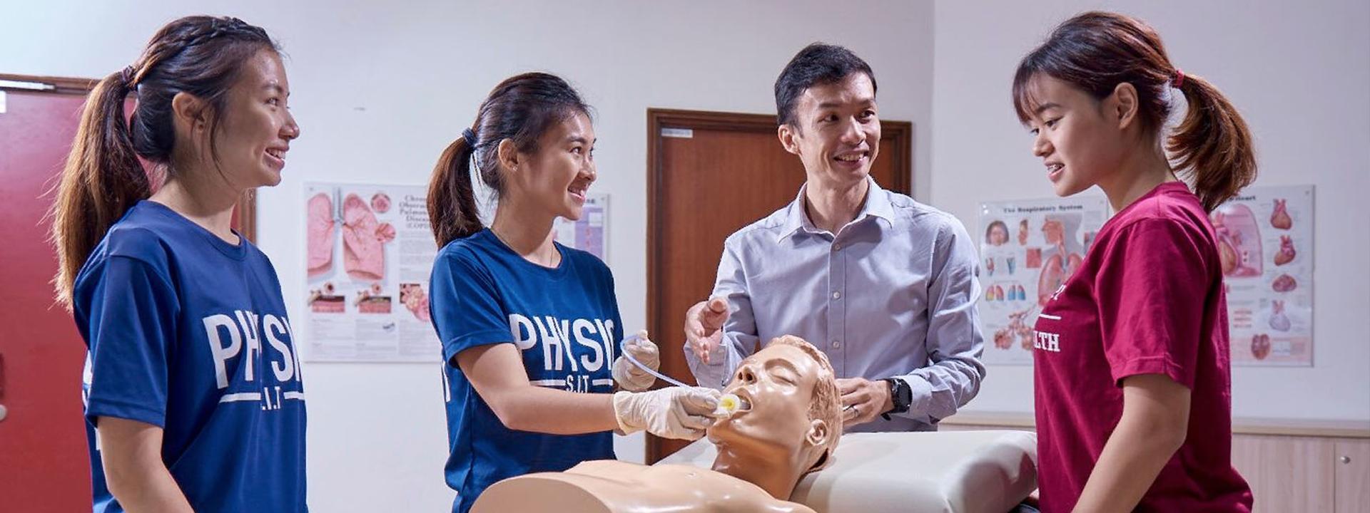Physiotherapy program showing an instructor teaching two students in 'PHYSIO S.I.T.' t-shirts, with a half body human model in the background.