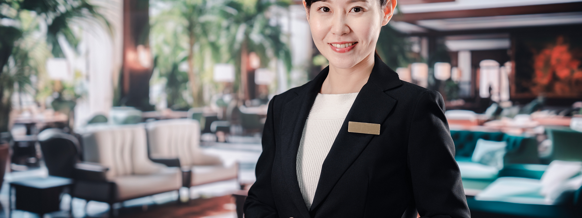 A smiling Hospitality and Tourism Management professional in a suit against a blurred hotel lobby background